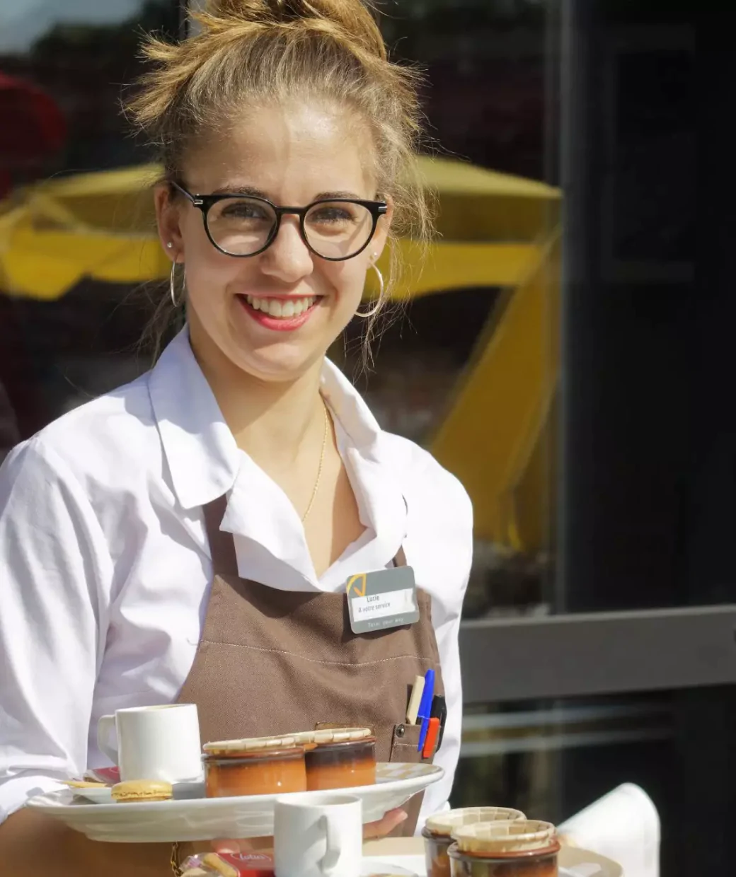 Camarera sonriente con bandeja de cafés en el exterior de un local.