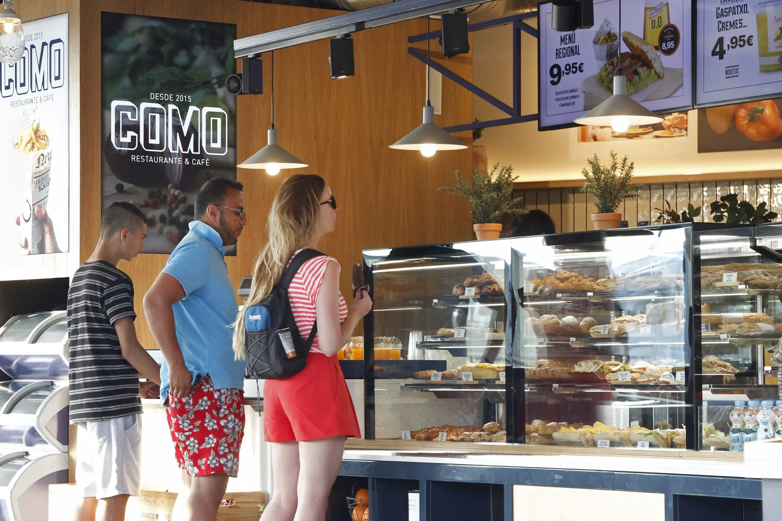 Clientes observando la vitrina de bollería en el mostrador de un restaurante-cafetería.