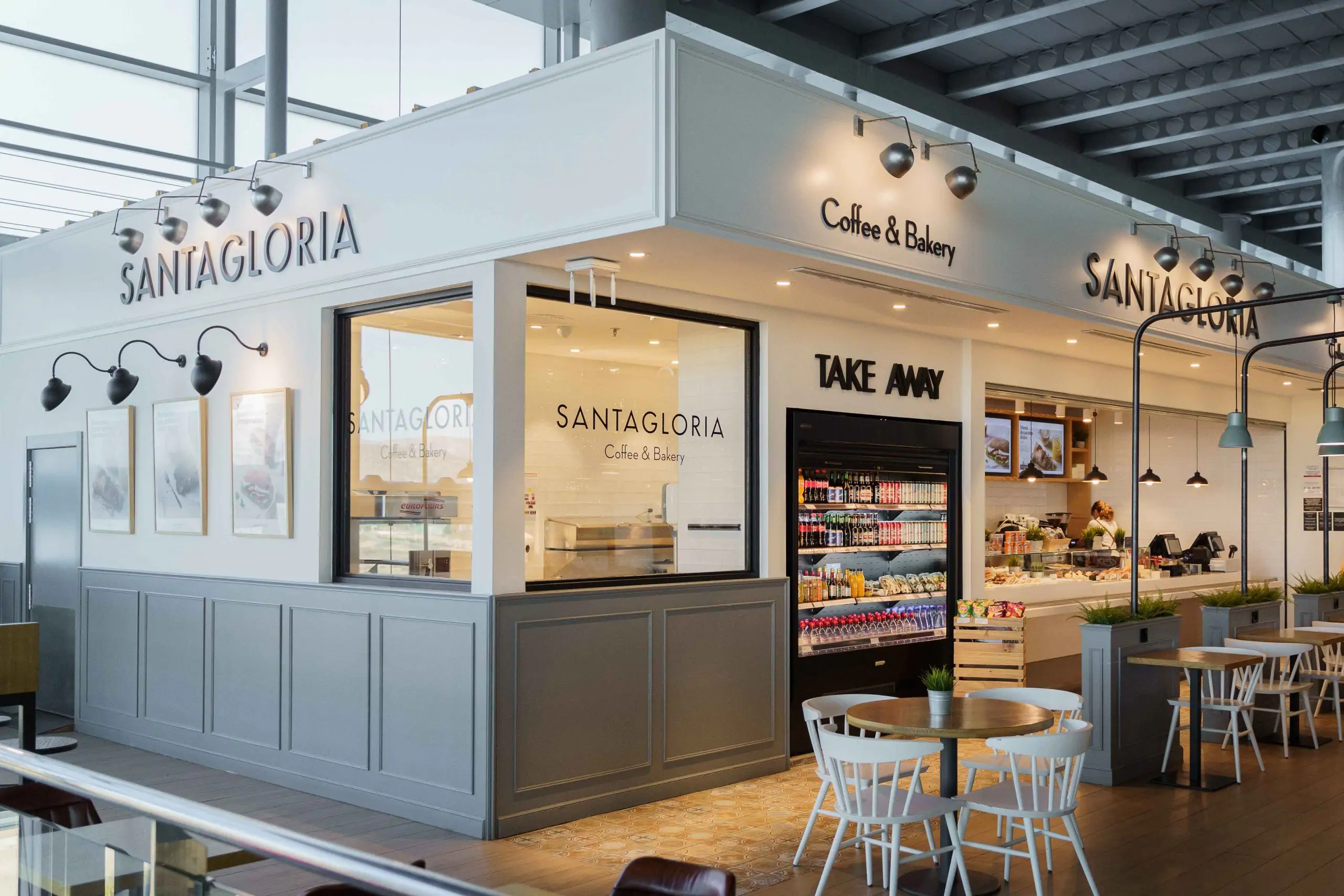 Fachada de cafetería Santagloria con zona de take away y mesas.