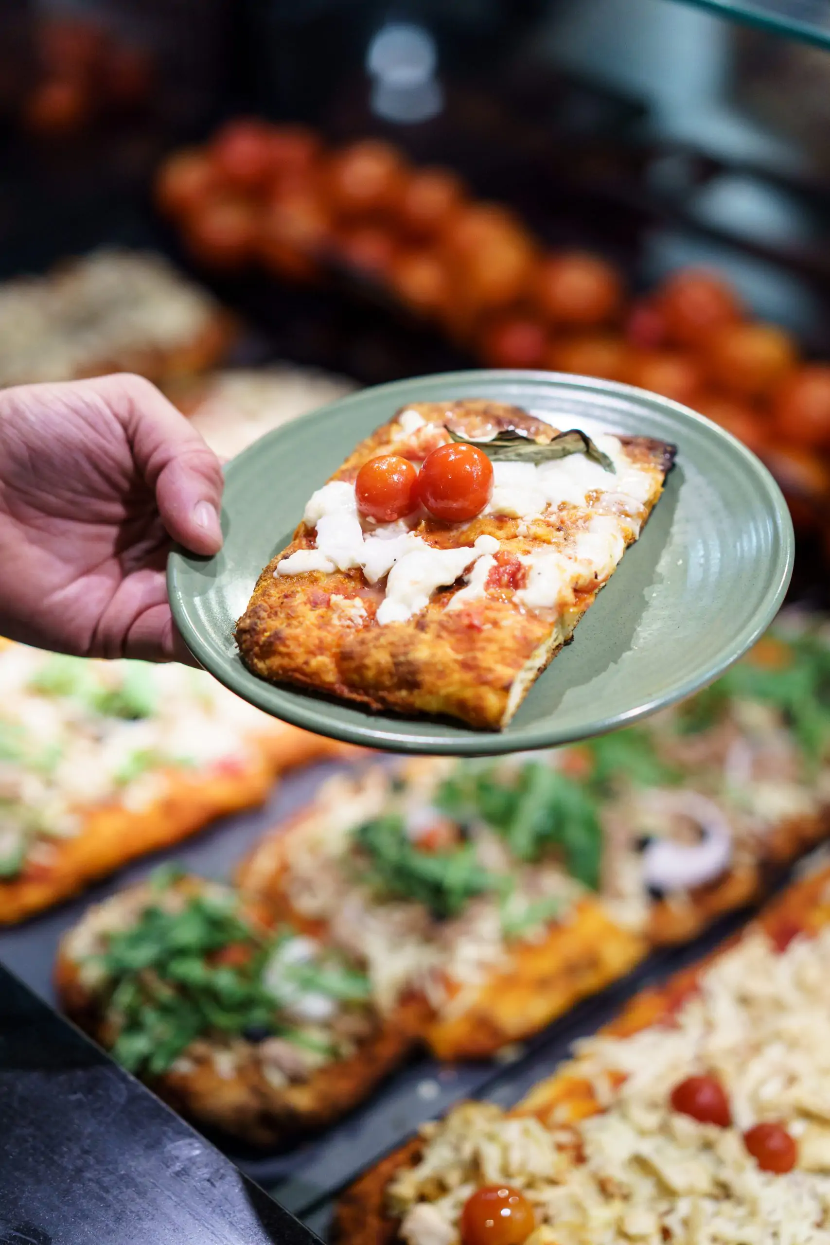 Porción de pizza artesanal servida en plato con tomates cherry y queso fundido.