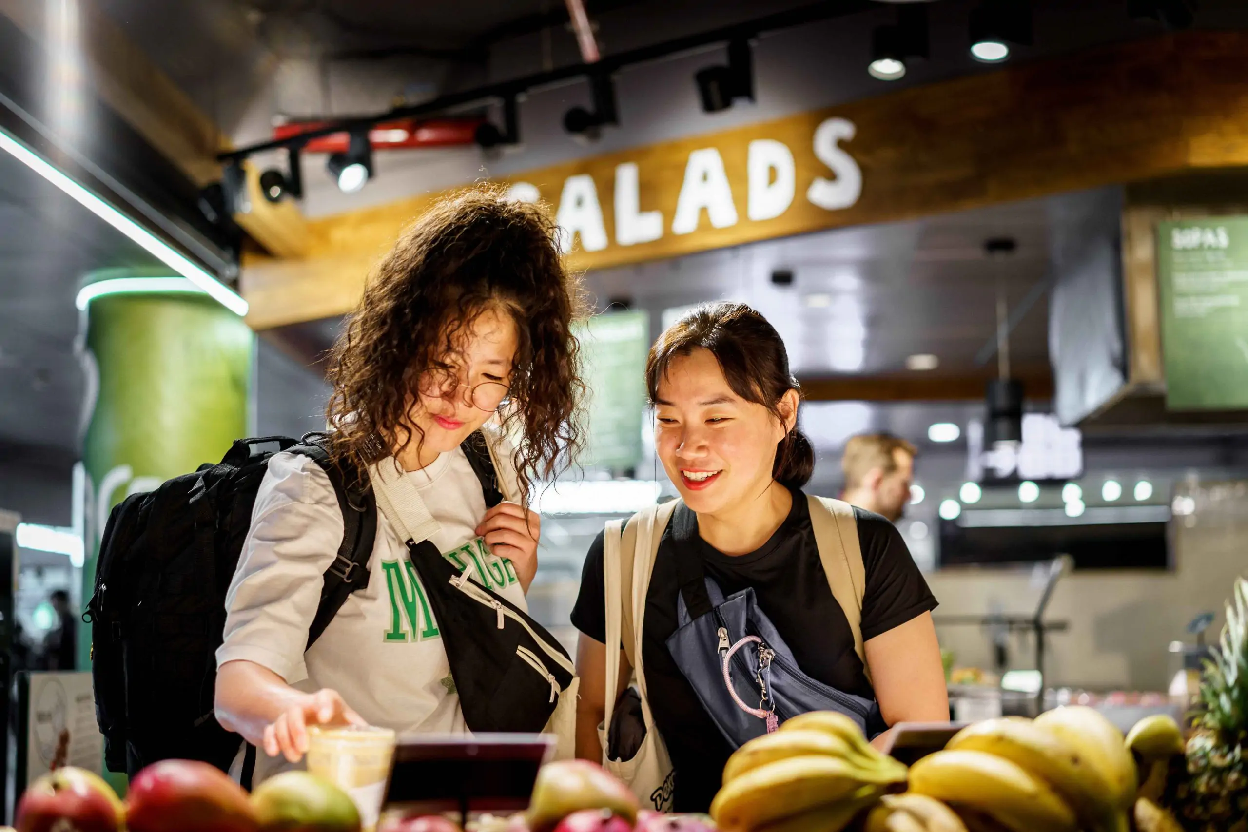 Dos mujeres eligiendo comida en un mostrador de ensaladas.