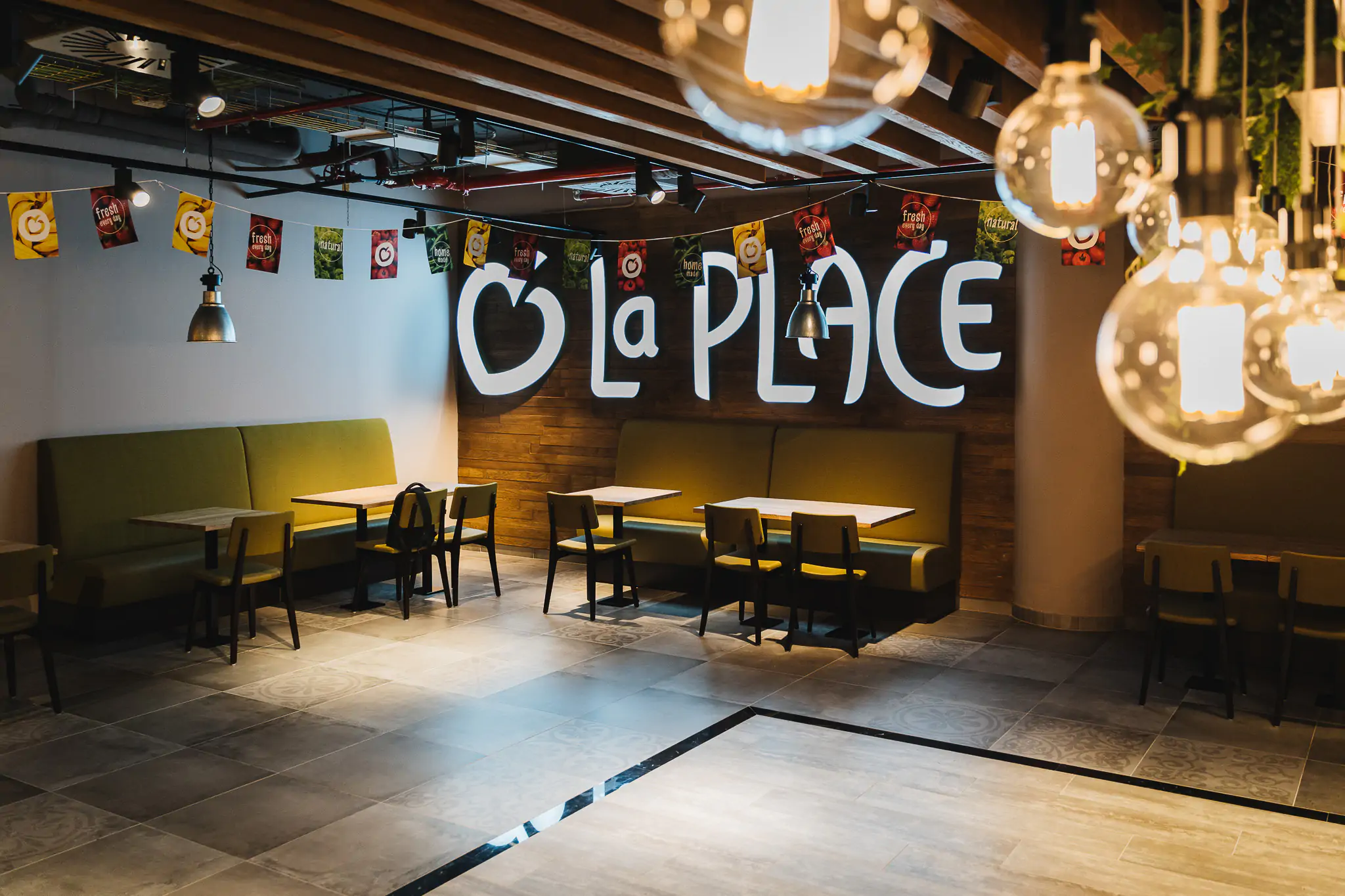 Zona de comedor de La Place con mesas y rótulo iluminado.