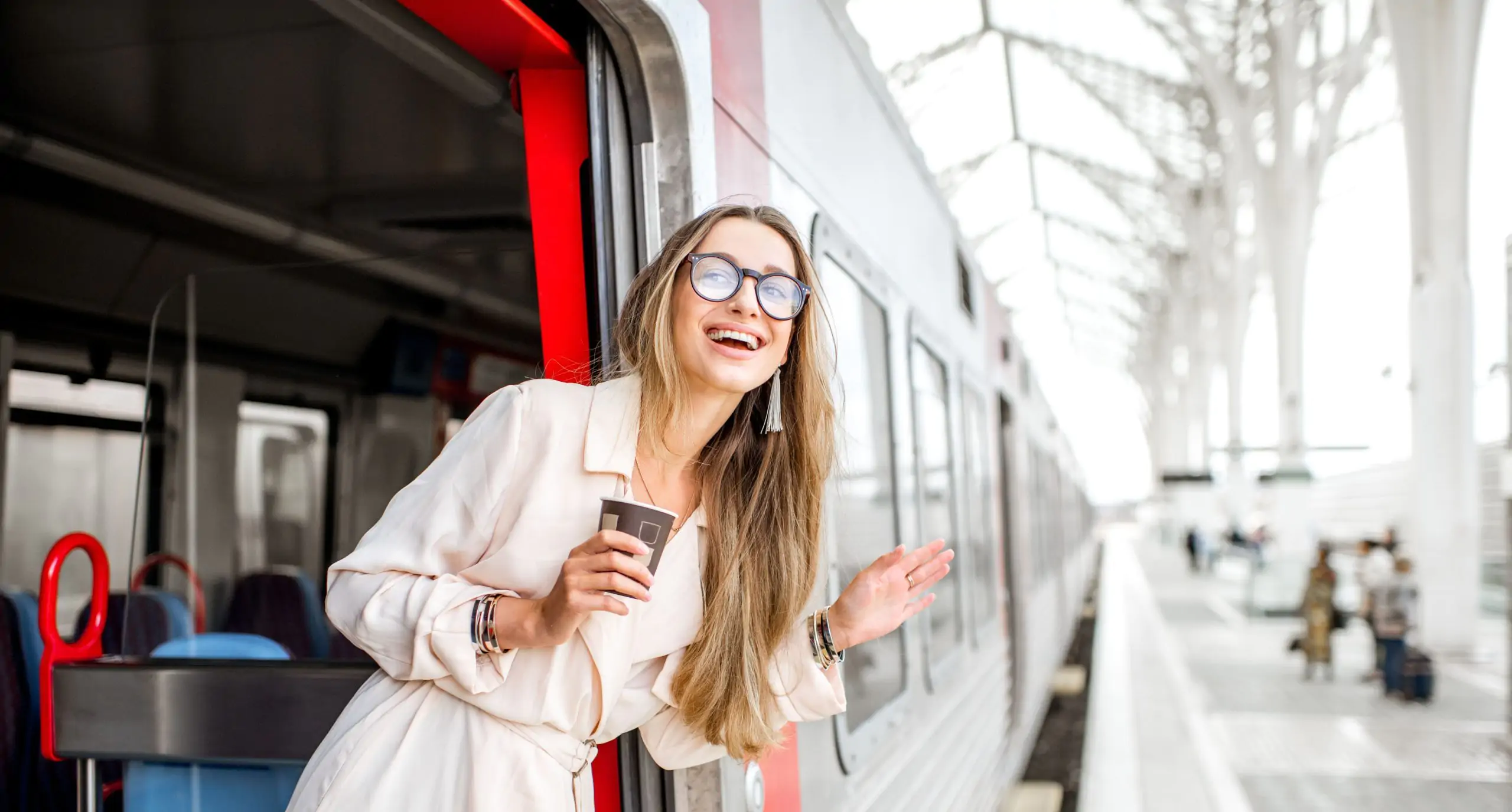 Mujer sonriendo y saludando desde la puerta de un tren en la estación.