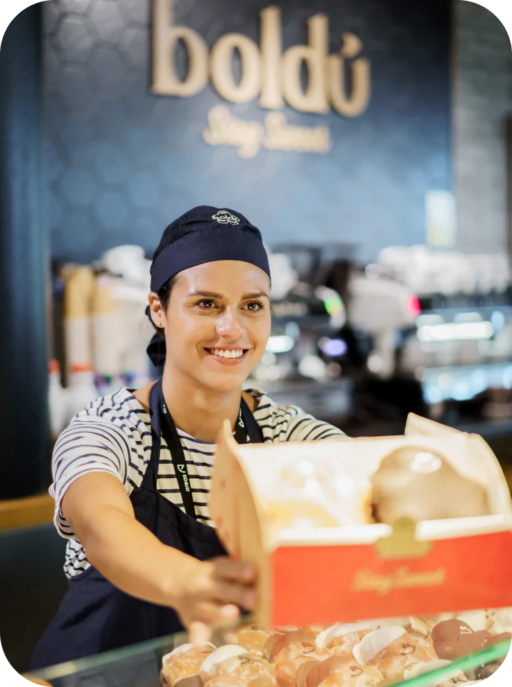Empleada de pastelería entregando una caja de dulces en el mostrador.